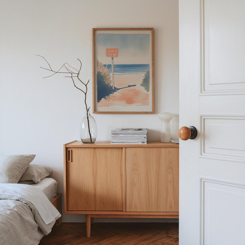 a serene bedroom scene with a wooden dresser, a framed beach sign, and a vase with branches.