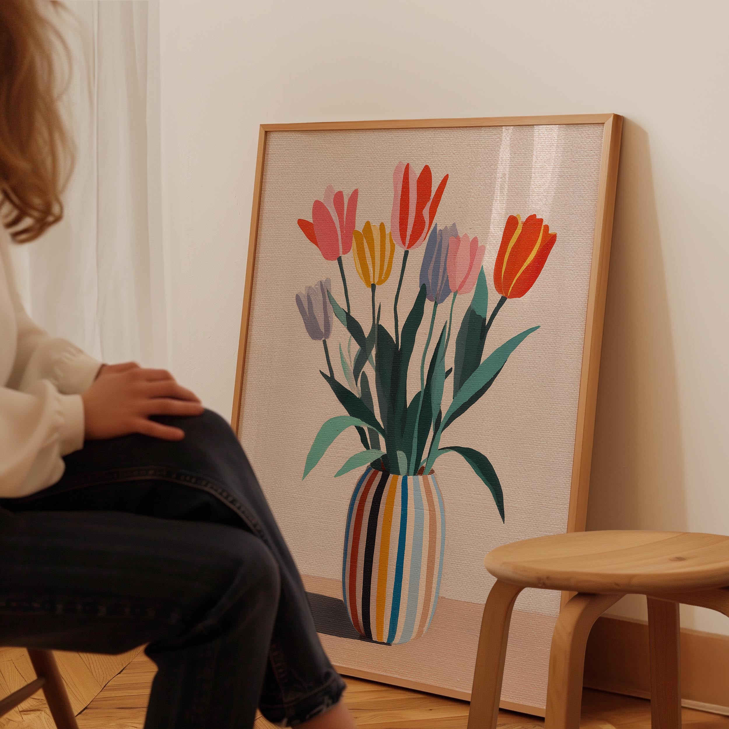 A person is sitting in front of a large framed painting depicting a vase with colorful tulips.