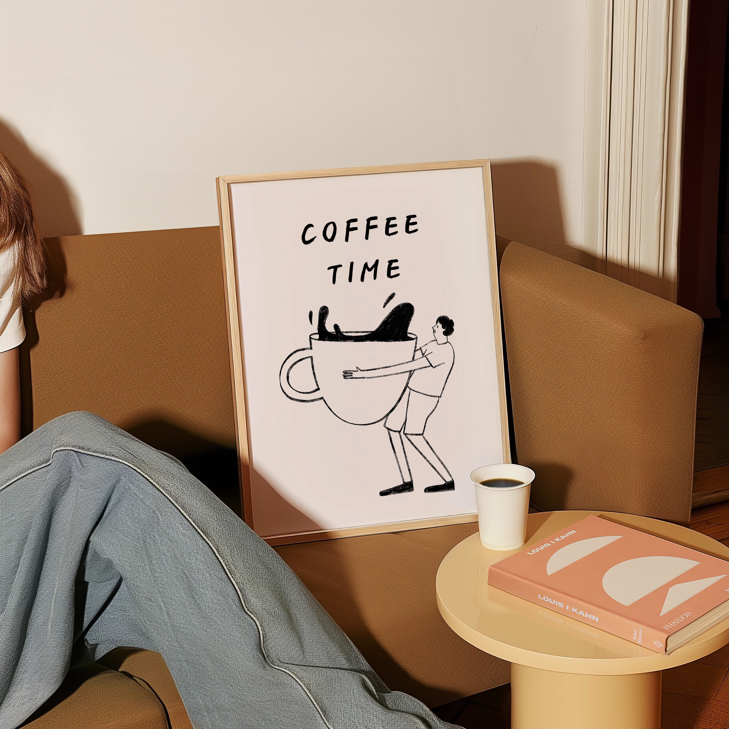 a framed poster with a cartoon illustration of a person holding a coffee mug, accompanied by the text "COFFEE TIME". The poster is displayed on a brown couch, with a person's legs visible in the foreground. In the background, there is a small table with a book and a cup of coffee.
