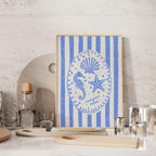a framed artwork with a blue and white design depicting a seahorse, starfish, and seashell, along with the text "summer vibes" written around the edges. The artwork is displayed on a shelf, surrounded by various kitchen items such as a bottle, cups, and a cutting board.