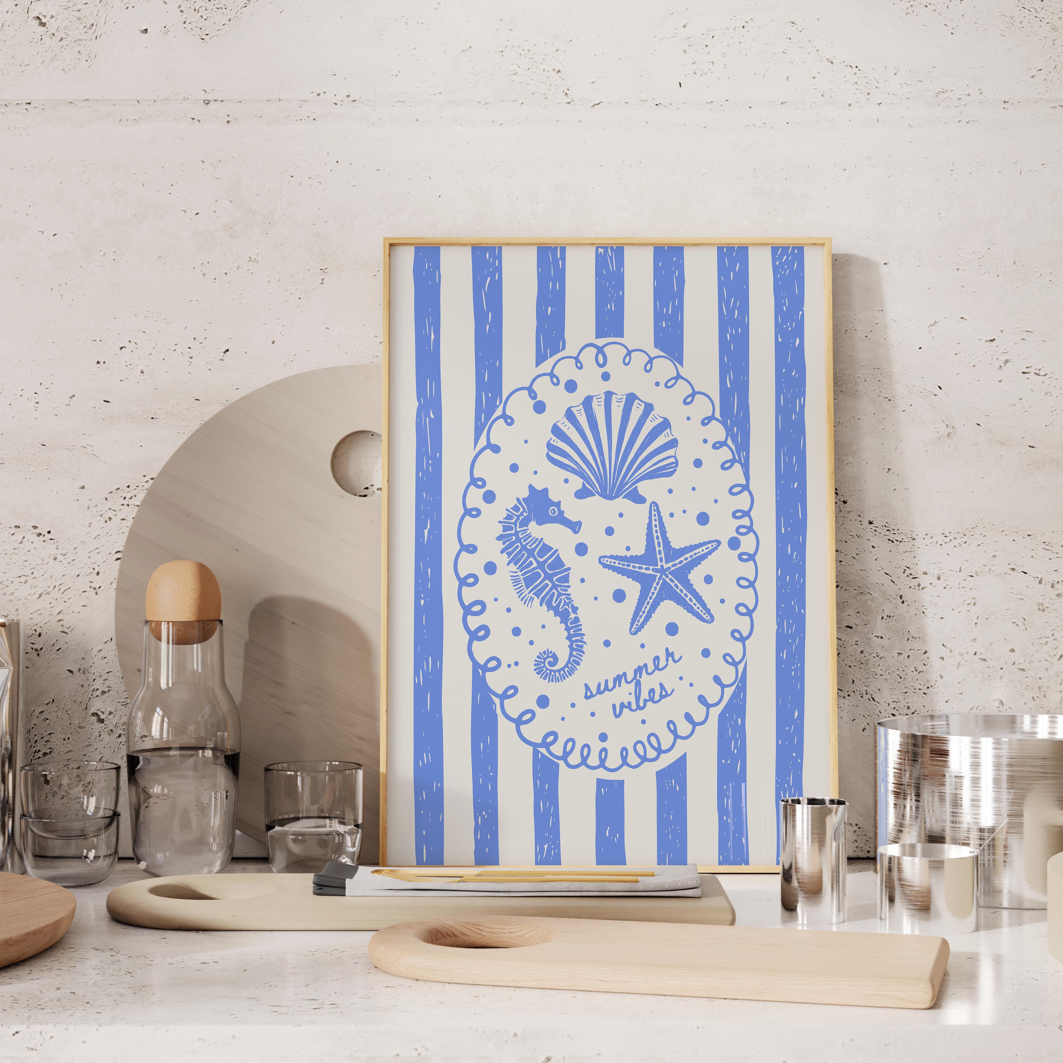 a framed artwork with a blue and white design depicting a seahorse, starfish, and seashell, along with the text "summer vibes" written around the edges. The artwork is displayed on a shelf, surrounded by various kitchen items such as a bottle, cups, and a cutting board.