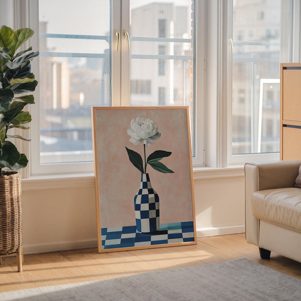 a large painting of a white flower in a checkered vase, placed on a wooden floor in front of a window overlooking a cityscape.