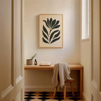a cozy corner of a room with a wooden desk, a framed abstract art piece on the wall, and a chair with a blanket draped over it.