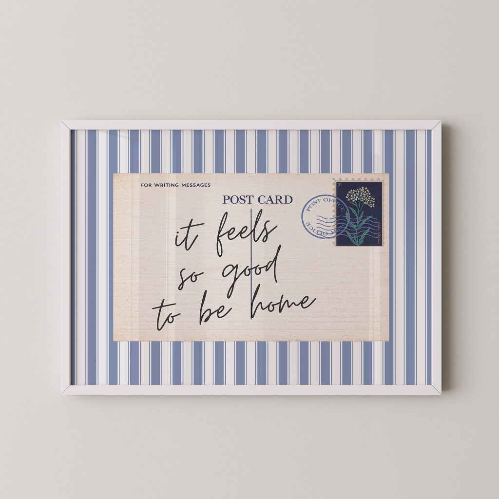 The image is a framed postcard with a blue and white striped border, featuring a handwritten message that reads "it feels so good to be home".