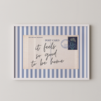 The image is a framed postcard with a blue and white striped border, featuring a handwritten message that reads "it feels so good to be home".