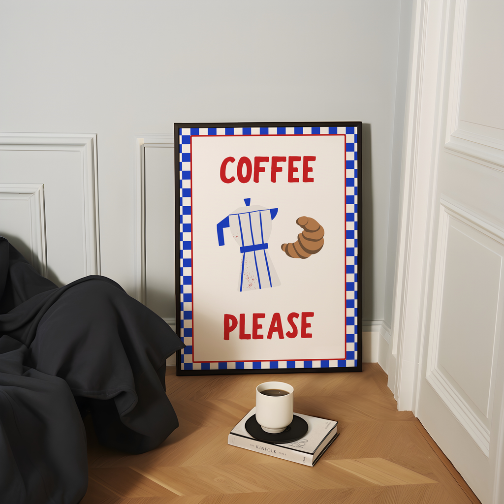 a framed sign that reads "COFFEE PLEASE" with an illustration of a coffee cup and croissants, placed on a wooden floor next to a book and a cup of coffee.