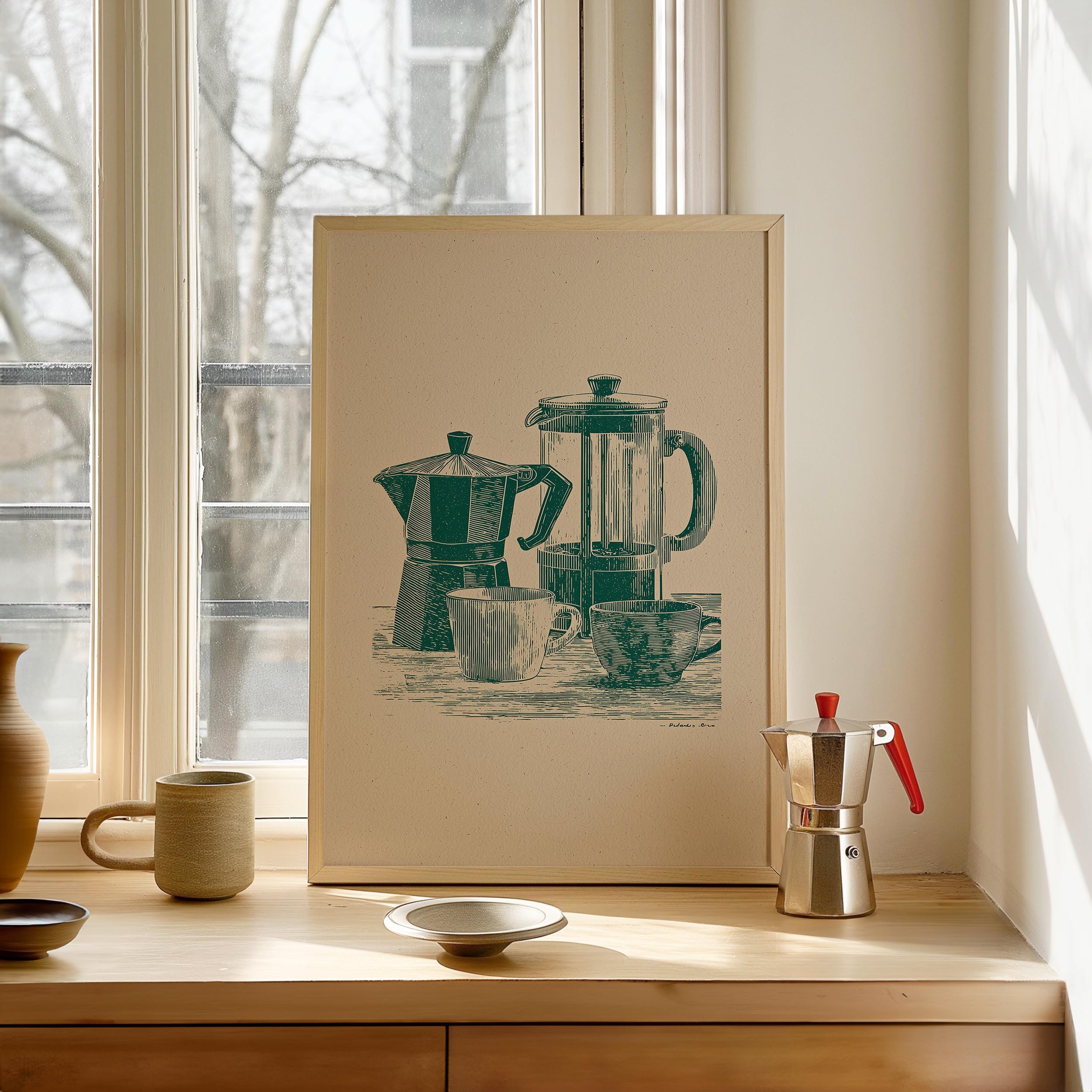a framed illustration of two coffee makers on a windowsill, with a small white bowl and a red coffee pot placed in front of the framed image.