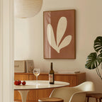 a dining room with a table set for two, a bottle of wine, and a framed abstract leaf-like artwork on the wall.