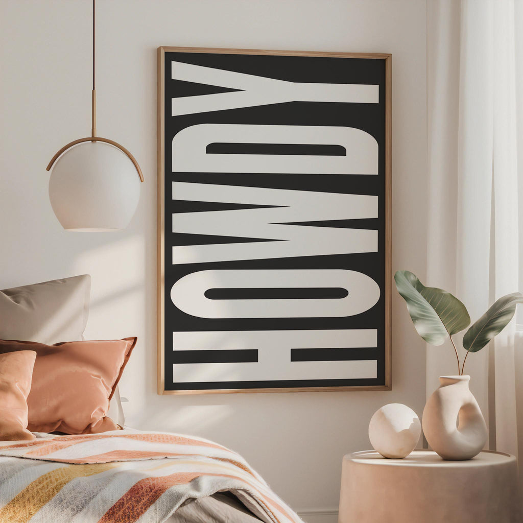 a bedroom with a large black and white text poster on the wall, a bed with colorful pillows, and a small side table with a vase and plant.