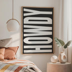 a bedroom with a large black and white text poster on the wall, a bed with colorful pillows, and a small side table with a vase and plant.
