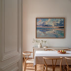a serene dining room with a white table and chairs, a vase of flowers, and a framed painting of a beach scene hanging on the wall.