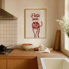 a kitchen counter with a framed poster of a red spaghetti noodle with a fork and a bowl of fruit, including oranges, on it.