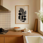 a kitchen counter with a bowl of oranges, a cutting board, and a vase of white flowers. Above the counter, there is a framed abstract art piece hanging on the wall.