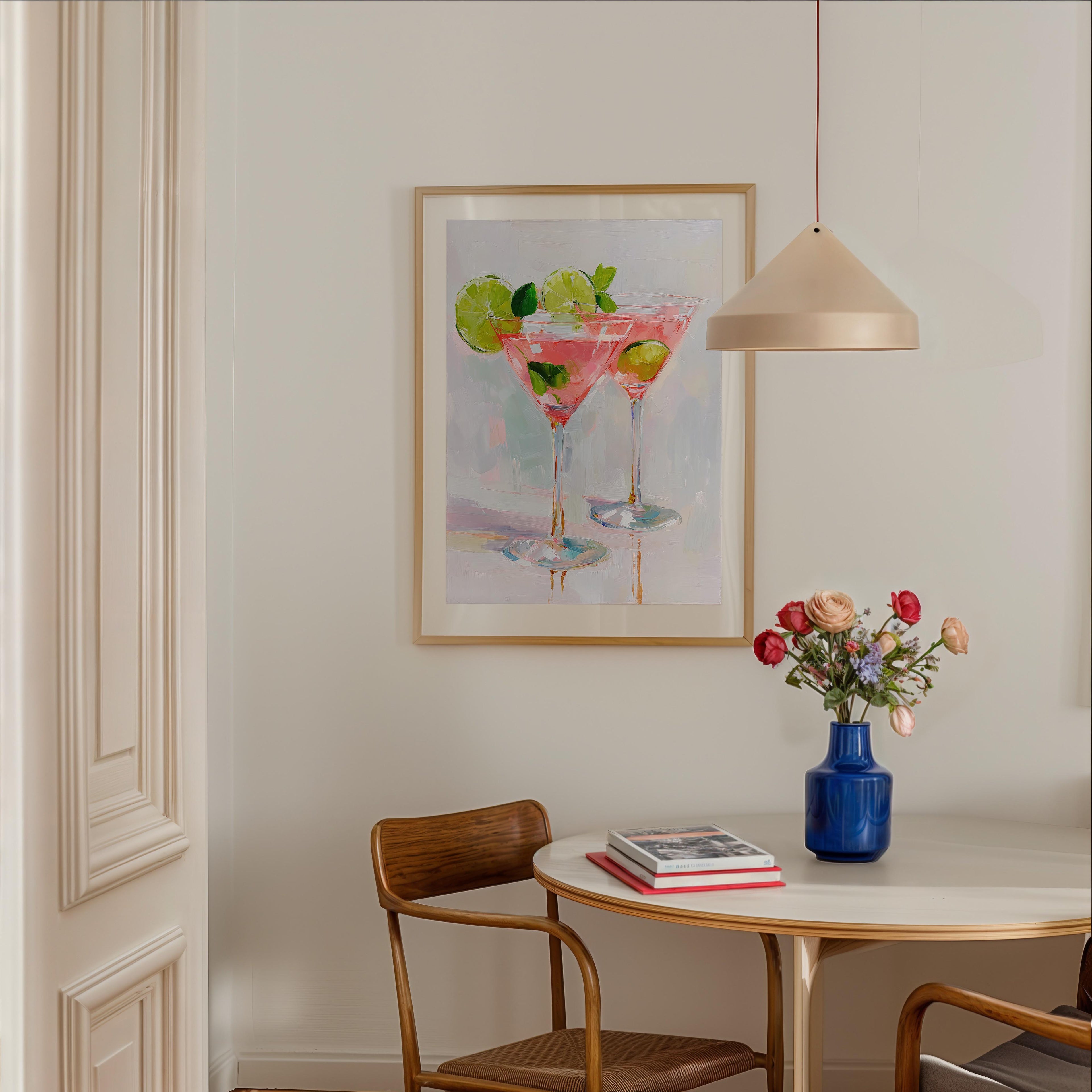 a dining area with a table, chairs, and a framed painting of two martini glasses with fruit on the wall.