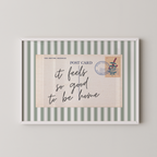 The image is a framed postcard with a handwritten message that reads "it feels so good to be home".