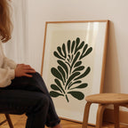 A person is sitting on a chair in front of a large framed print of a stylized plant or flower design.