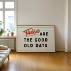 A large framed sign with the text "These are the good old days" is displayed in a room with a window and a plant.