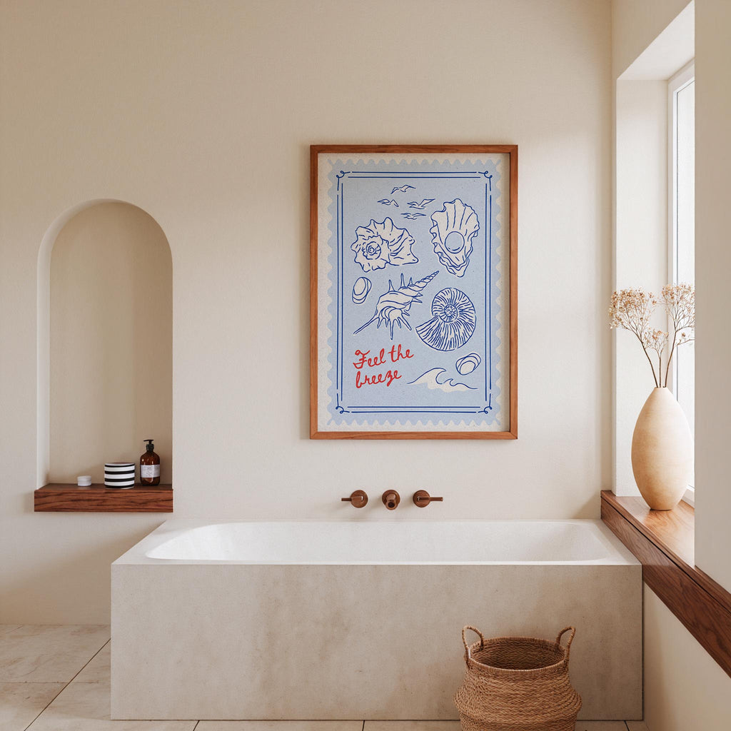 a bathroom with a large framed poster of a blue and white illustration hanging on the wall above a white bathtub. The poster depicts a seashell and a rose, adding a coastal touch to the room. The bathroom also includes a window, a shelf with toiletries, and a woven basket, creating a cozy and inviting atmosphere.