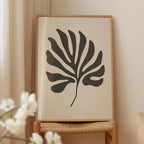 a framed artwork of a leaf-like design in black and white, displayed on a wooden stand.