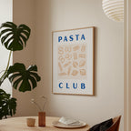 a framed poster with the text "PASTA CLUB" hanging on a wall, surrounded by various pasta-related illustrations. The poster is placed above a dining table with a vase of flowers and a cup.