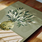 a vase filled with green leaves and branches, placed on a wooden surface.