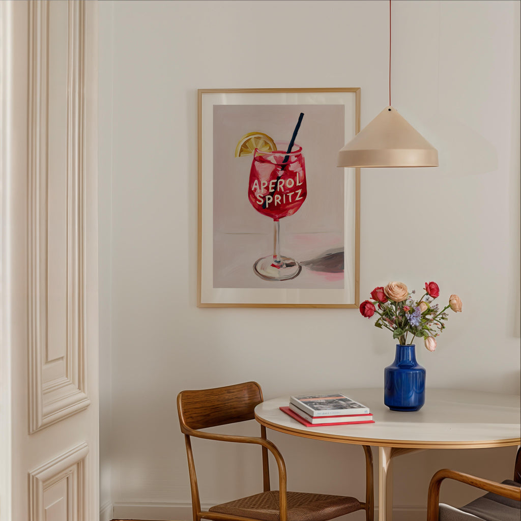 a dining area with a table, chairs, and a framed poster of a drink on the wall.