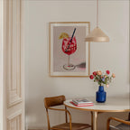 a dining area with a table, chairs, and a framed poster of a drink on the wall.