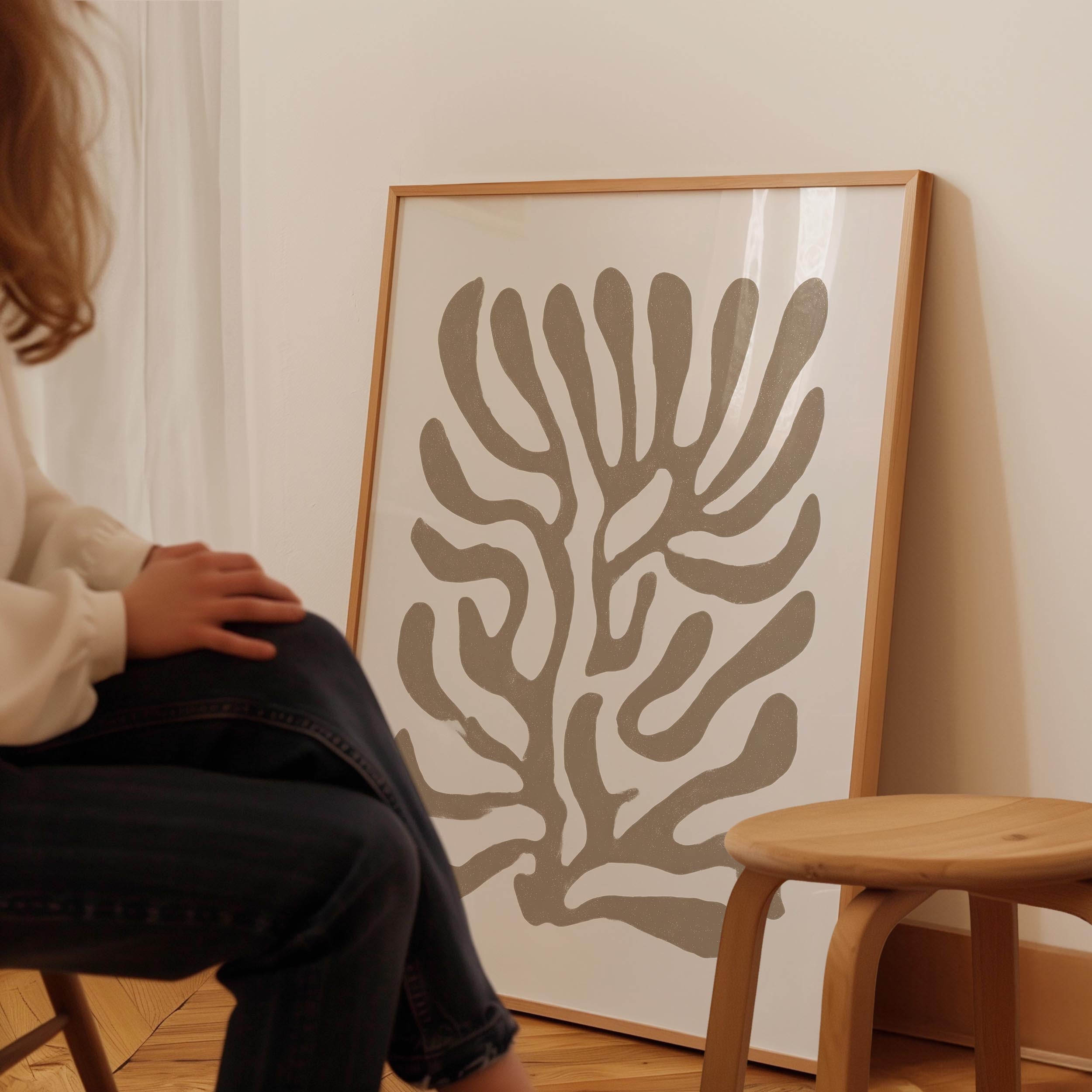 A person is sitting on a chair in front of a large abstract art piece on a wall.