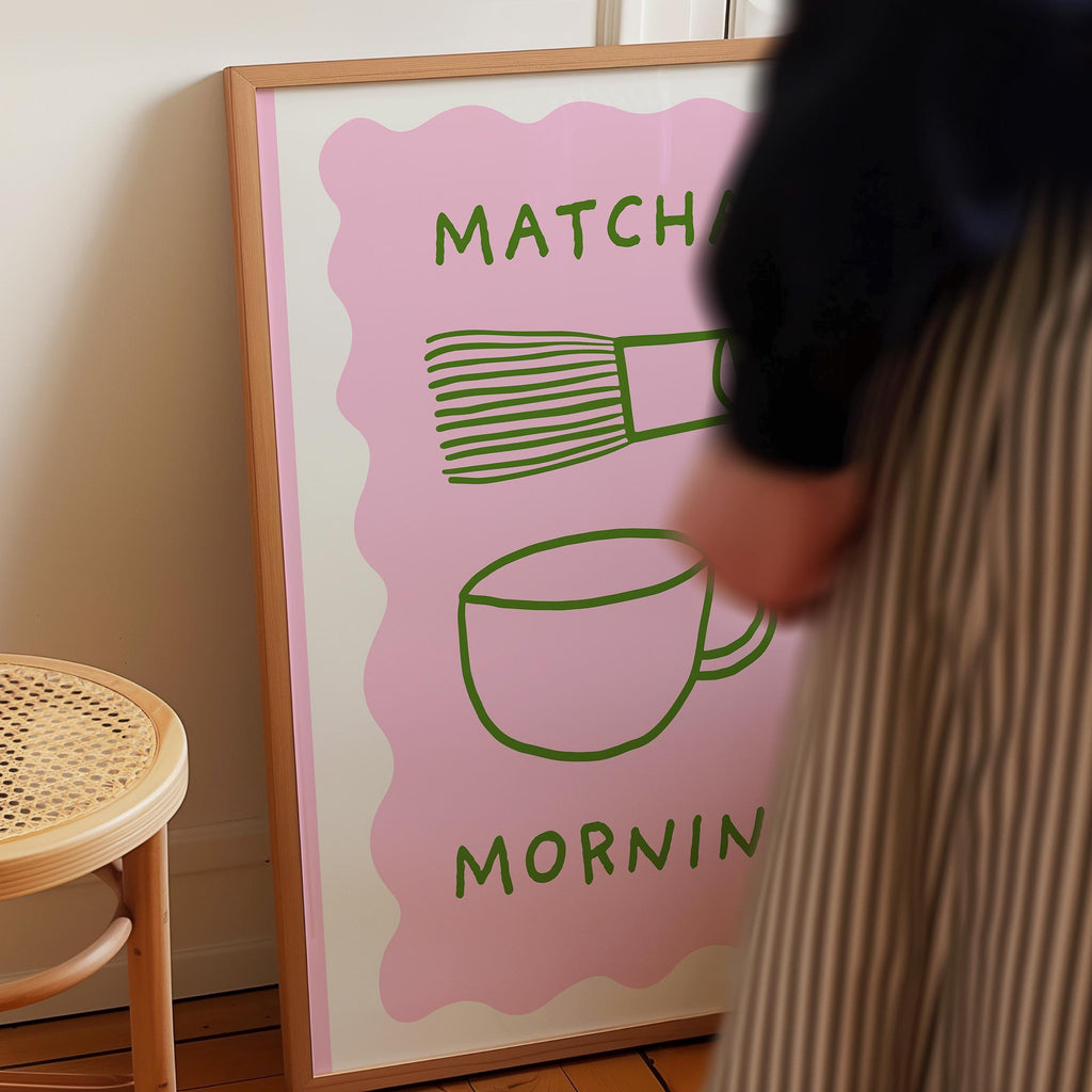 a person standing next to a framed poster with a pink background and green text.