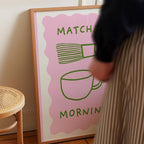 a person standing next to a framed poster with a pink background and green text.