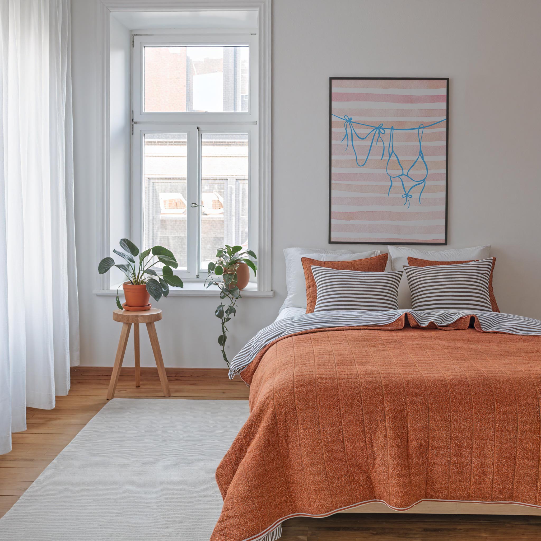 a cozy bedroom with a large bed, a wooden stool with a potted plant, and a framed artwork on the wall.