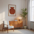 a cozy corner of a room with a white armchair, a wooden sideboard, a lamp, and a potted plant. The room has a minimalist and modern design, with a large window allowing natural light to fill the space.