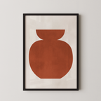 a simple, abstract design of a large orange shape, which appears to be a vase or container, displayed in a black frame on a white wall.