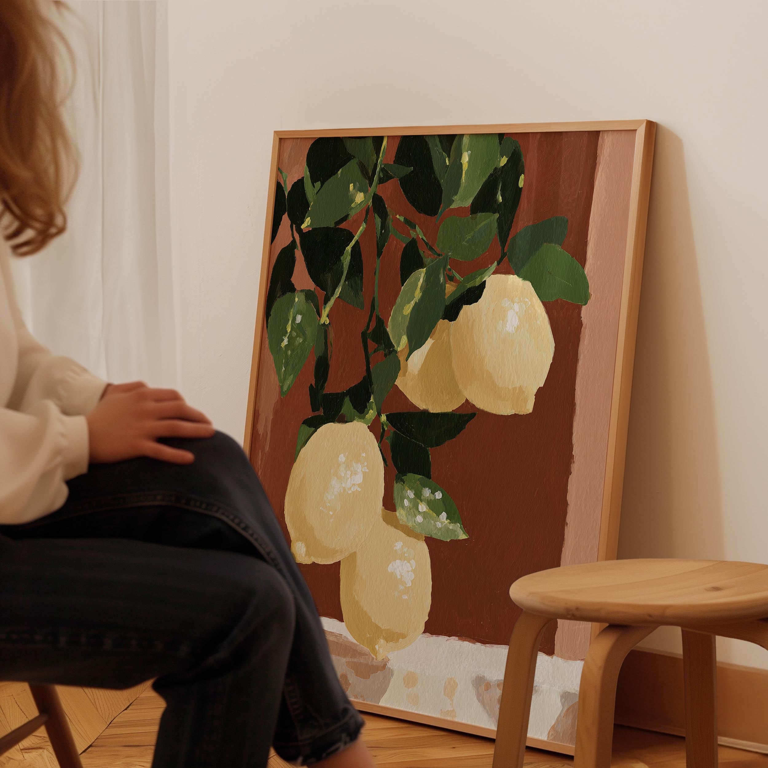A person is sitting in front of a painting that depicts a bunch of lemons hanging from a tree.