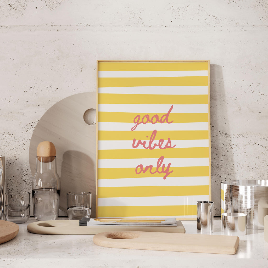 a yellow and white striped poster with the text "good vibes only" displayed on it, placed on a countertop with various kitchen items such as a bottle, cups, and a cutting board.