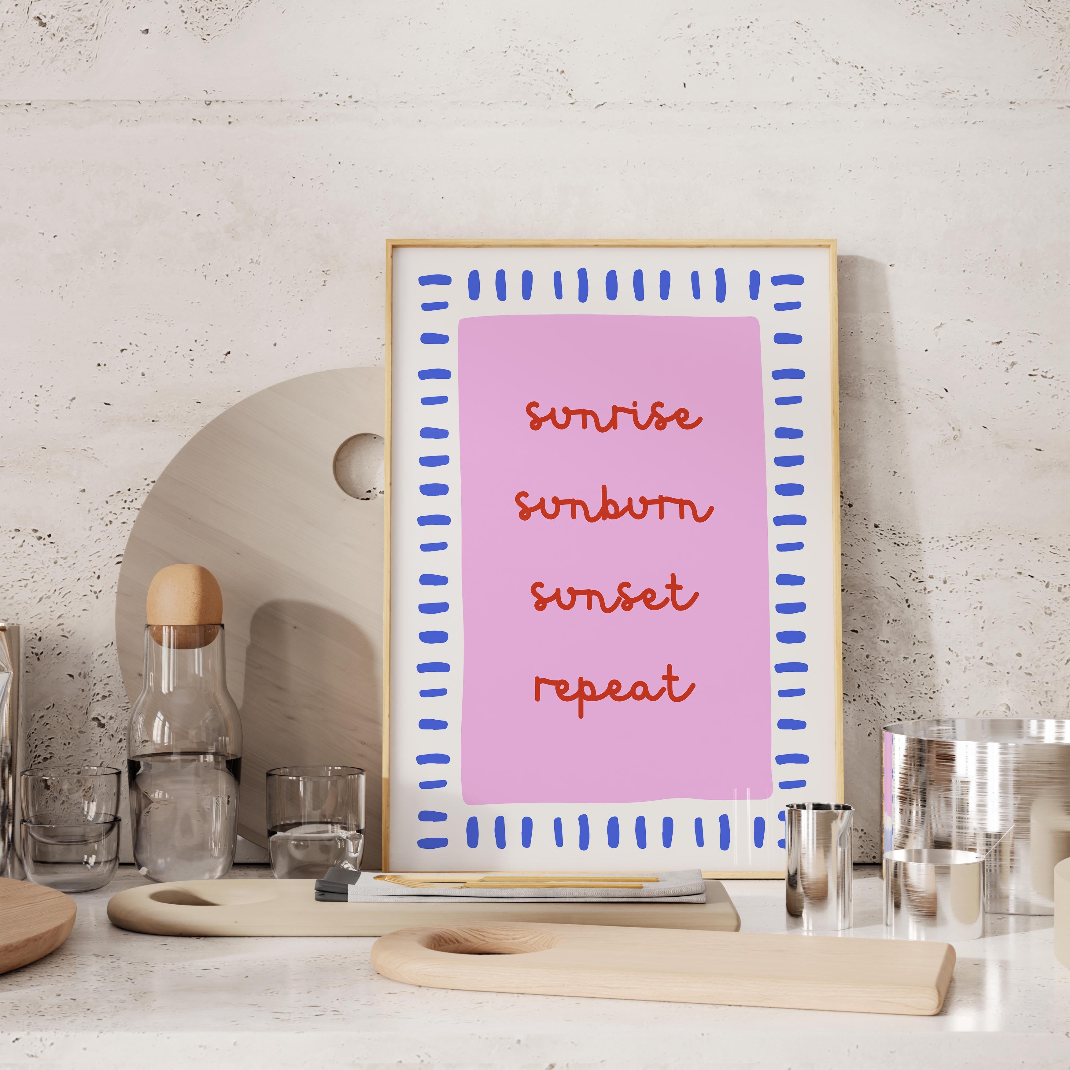 a pink framed poster with the words "sunrise, sunset, repeat" written on it, placed on a countertop next to various kitchen items such as a bottle, cups, and a cutting board.