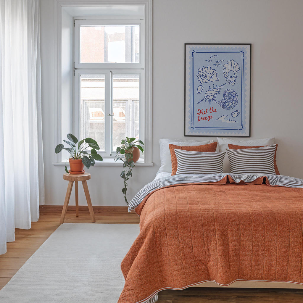 a cozy bedroom with a large bed, a wooden stool with a potted plant, and a framed artwork on the wall.