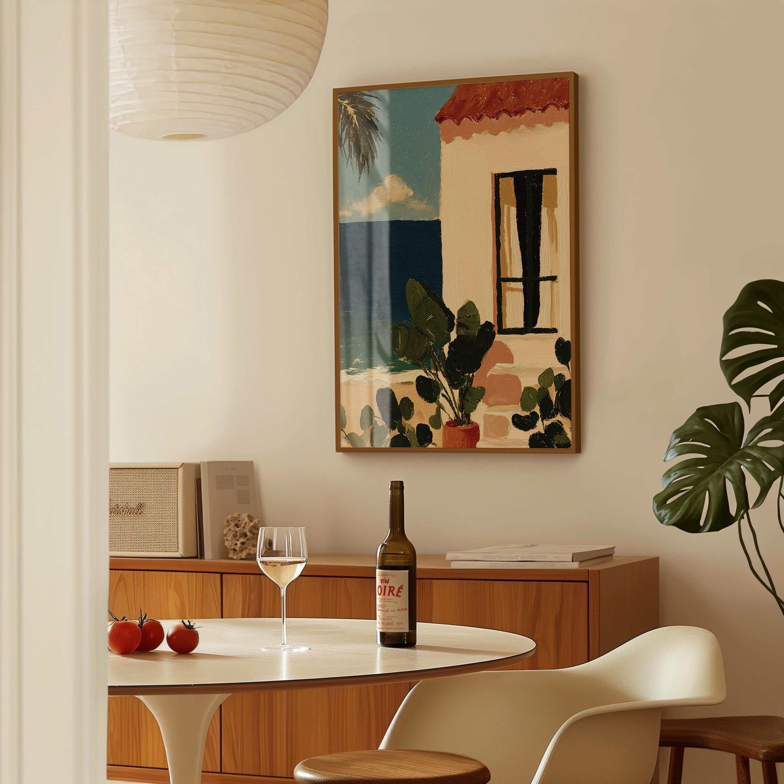 a cozy dining area with a table set for two, featuring a bottle of wine, a glass, and a plate of fruit. A framed painting of a tropical scene hangs on the wall above the table, adding a touch of color and artistry to the space.