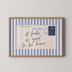 The image is a framed print with a blue and white striped border, featuring a handwritten message that reads "it feels so good to be home".