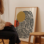 A person is sitting on a chair in front of a large abstract painting with a black and white spiral design and a yellow circle.