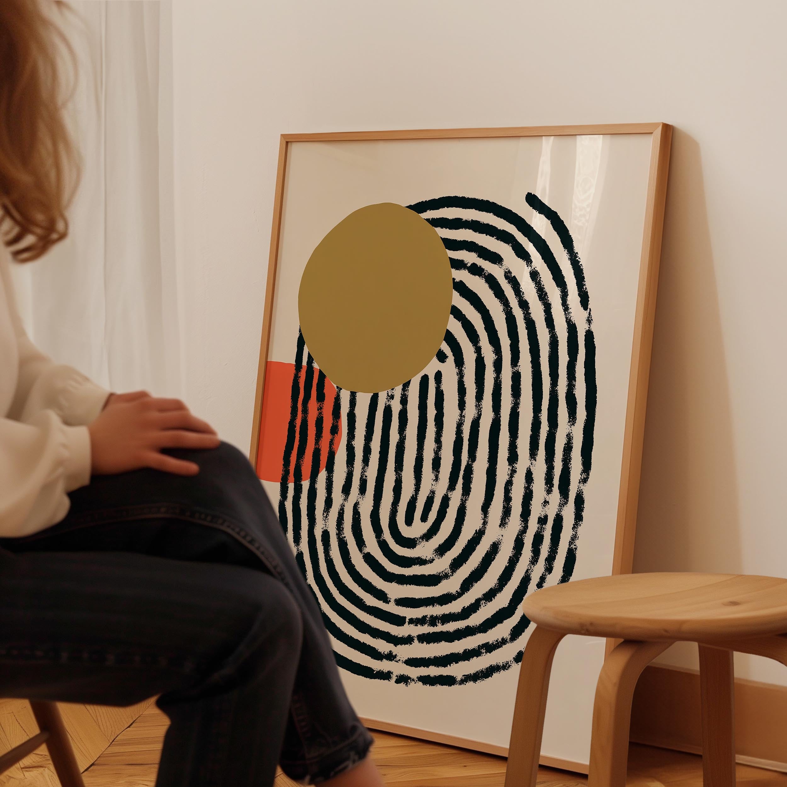 A person is sitting on a chair in front of a large abstract painting with a black and white spiral design and a yellow circle.