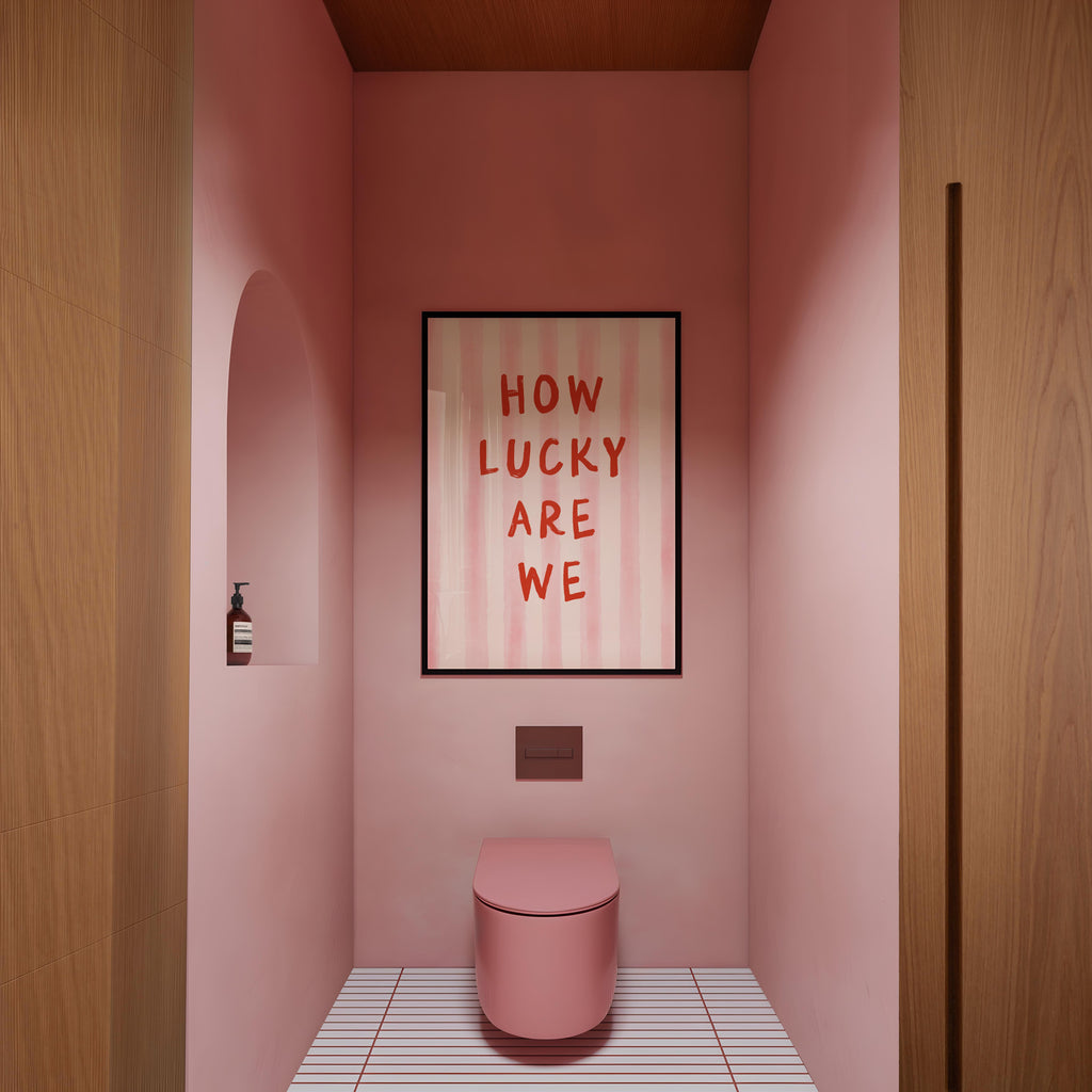 a bathroom with a pink toilet and a framed text that reads "HOW LUCKY ARE WE".
