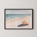 A framed watercolor painting depicting a seashell resting on a sandy beach, with the ocean visible in the background.
