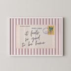 The image is a framed postcard with a handwritten message that reads "it feels so good to be home".