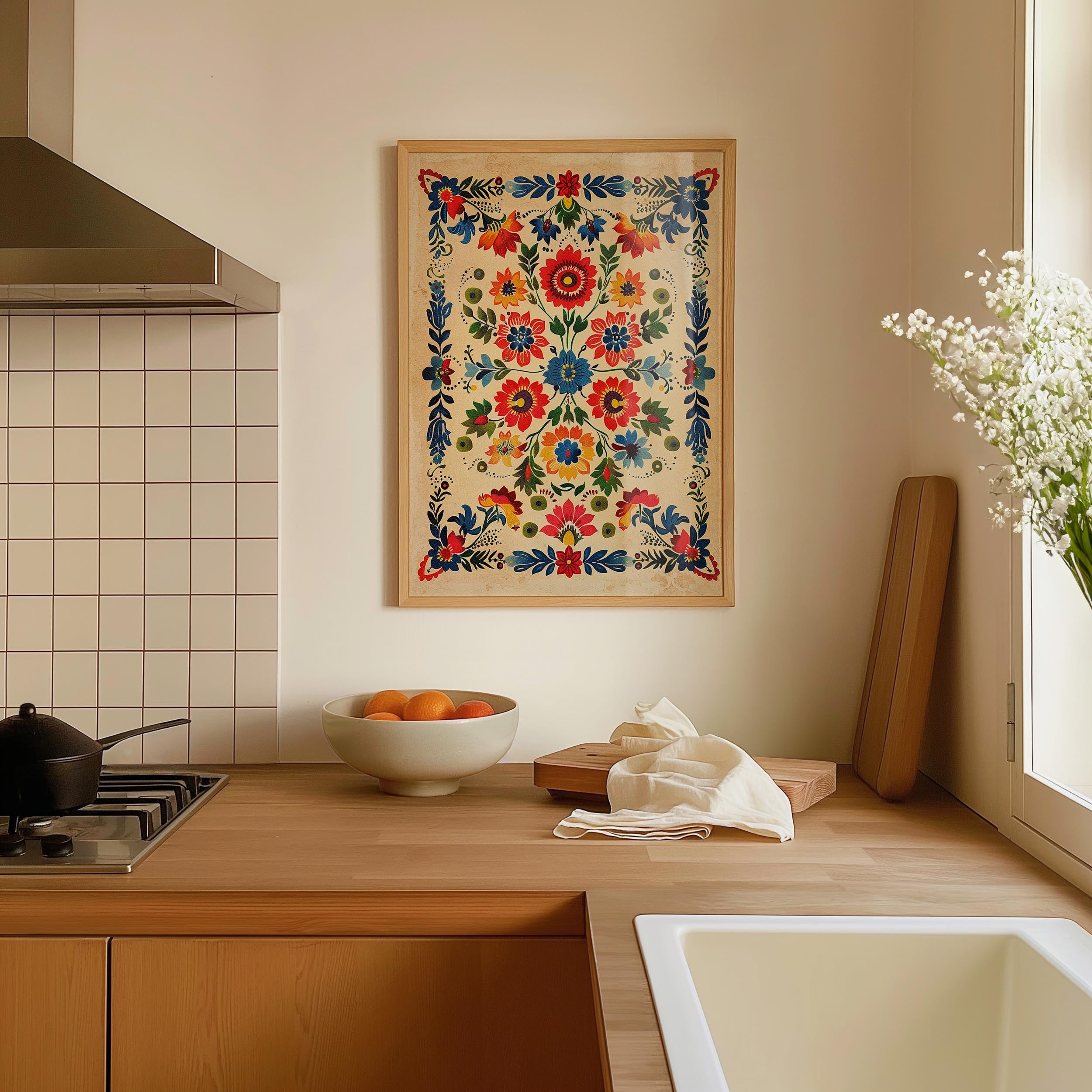 a kitchen counter with a bowl of fruit, a vase of white flowers, and a framed floral print hanging on the wall above the counter.