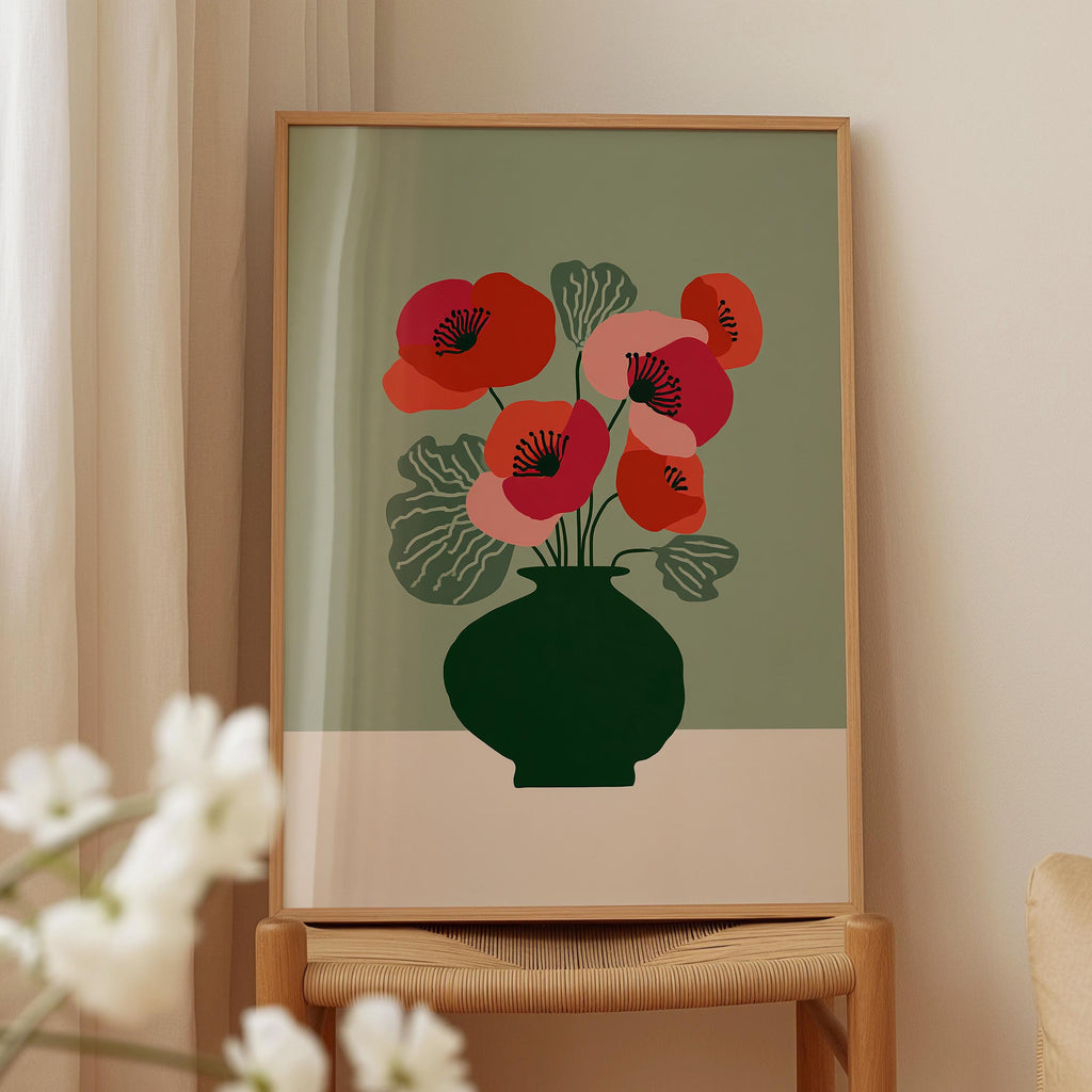 a framed print of a vase with red flowers on a green background, placed on a wooden chair.