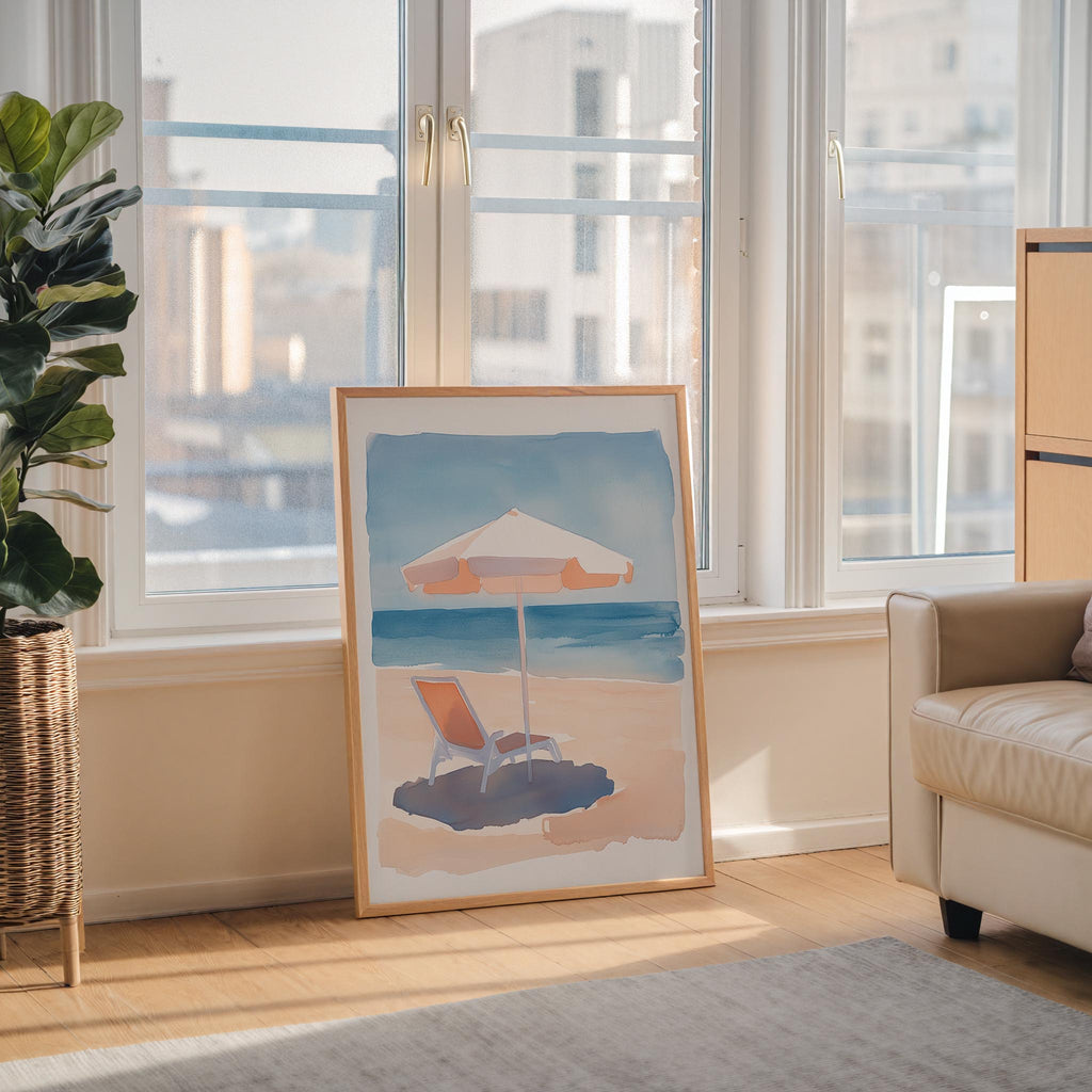 a large framed painting depicting a beach scene with a beach umbrella and a lounge chair, placed on a wooden floor in a room with large windows overlooking a cityscape.