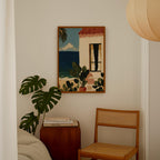 a cozy corner of a room with a painting of a beach scene hanging on the wall, a wooden chair, a small table with books, and a large monstera plant.