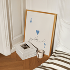 a framed poster with a heart and a question written on it, placed on a wooden floor next to a stack of books and a coffee mug.