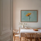 a dining room with a white table and chairs, a vase of flowers, and a framed painting of a yellow flower on the wall.